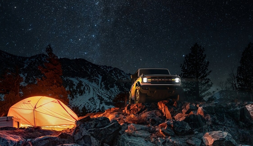 Ford Bronco climbing over rocks at a camp site at night